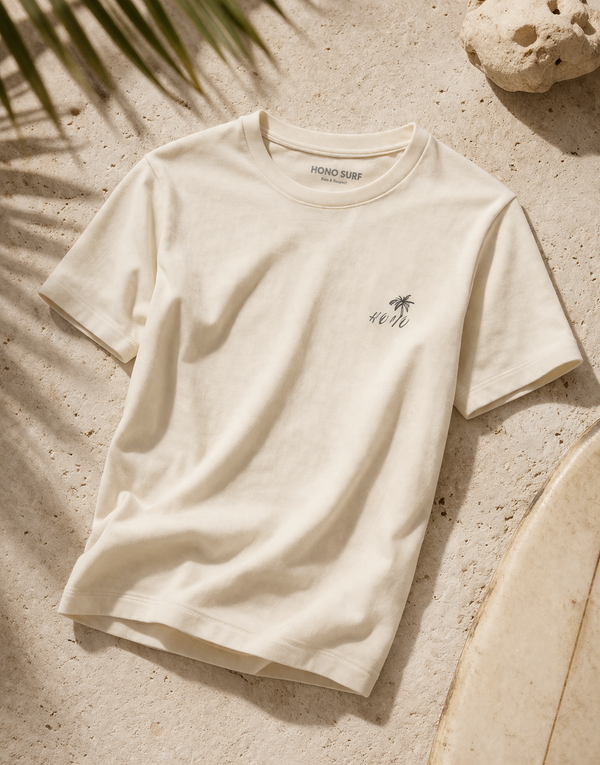 T-shirt femme beige naturel HONO SURF en coton bio, coupe ajustée, posé sur sable avec ambiance surf et lumière naturelle