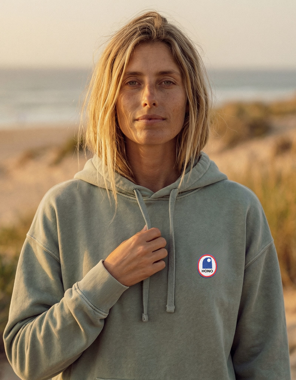 Femme portant un sweat à capuche oversize vintage Ocean Grey HONO sur la plage – hoodie surfwear durable en coton biologique-vêtement de surf