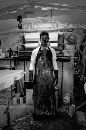 Shaper HONO dans son atelier de fabrication de planches de surf, équipé de protections et travaillant des matériaux, illustrant un savoir-faire artisanal et une production de boards éco-responsables en France.