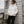 Doudoune blanche chaude en matières recyclées HONO, style surfwear, portée par une femme devant une cabane de pêcheur avec du bois et un poêle à bois.