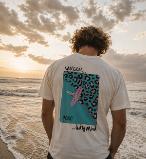 T-shirt surf blanc HONO x Gwendoline Le Ray avec illustration Wild Child Salty Mind dans le dos, porté face à l’océan au coucher du soleil