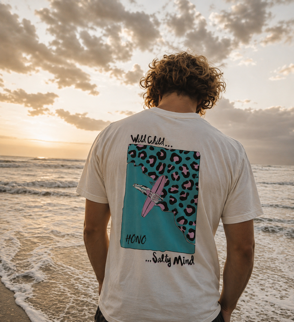 T-shirt surf blanc HONO x Gwendoline Le Ray avec illustration Wild Child Salty Mind dans le dos, porté face à l’océan au coucher du soleil