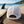 Dos de la casquette surf trucker blanche recyclée HONO avec fermeture snapback réglable, posée sur une table en bois face à l'océan à côté d'une planche de surf.