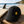 Casquette surf noire recyclée HONO avec broderie jaune posée sur une table en bois face à l'océan, à côté d'une planche de surf, dans une ambiance bord de mer lumineuse