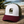 Casquette surf trucker recyclée HONO avec logo brodé kaki, panneau avant blanc, visière bordeaux et arrière en mesh kaki recyclé, photographiée en extérieur sur une table en bois face à l'océan.