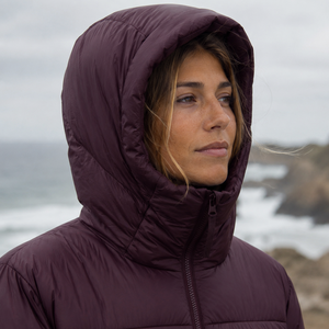Doudoune chaude en nylon recyclé HONO Surfwear bordeaux portée par une femme, capuche relevée face à l’océan