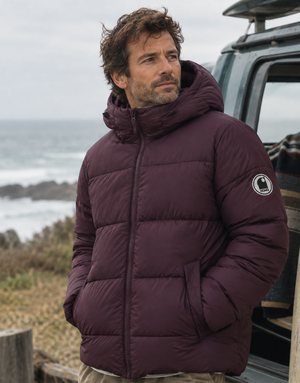 Doudoune chaude en nylon recyclé HONO Surfwear bordeaux portée par un homme face à l’océan