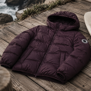 Doudoune chaude en nylon recyclé HONO Surfwear bordeaux posée sur une terrasse en bois face à l’océan