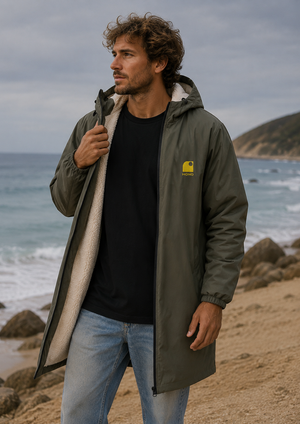 Imperméable chaud kaki HONO doublé polaire avec capuche et broderie jaune, porté par un homme sur la plage, surfwear bio écoresponsable et marque surf française