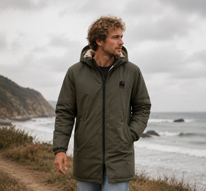Imperméable kaki HONO doublé polaire avec capuche et broderie noire, porté par un homme face à la mer, surfwear bio écoresponsable et marque furf rançaise
