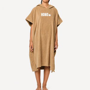 Poncho de surf beige en coton bio HONO avec gros logo brodé, porté par une femme, vue de face, surfwear français durable et éco-responsable