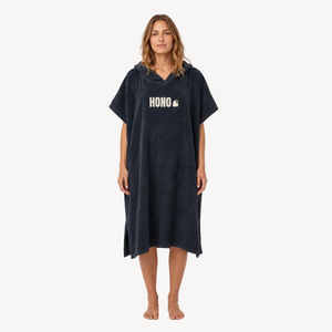 Poncho de surf noir en coton bio HONO avec logo blanc, porté par une femme, vue de face, surfwear français durable et éco-responsable