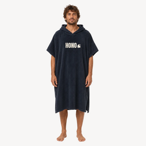 Poncho de surf noir en coton bio HONO avec logo blanc brodé, porté par un homme, vue de face, surfwear français durable et éco-responsable