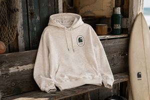 Sweat  surf à capuche écru HONO avec logo vert et noir, posé sur un banc dans un univers surf, surfwear bio écoresponsable et marque française