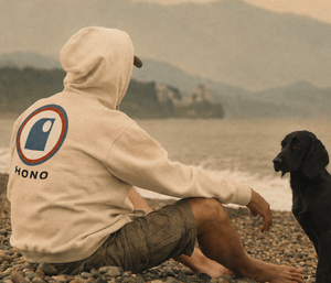 Sweat beige HONO à logo vintage porté par un homme sur une plage avec son chien – surfwear éco-responsable français