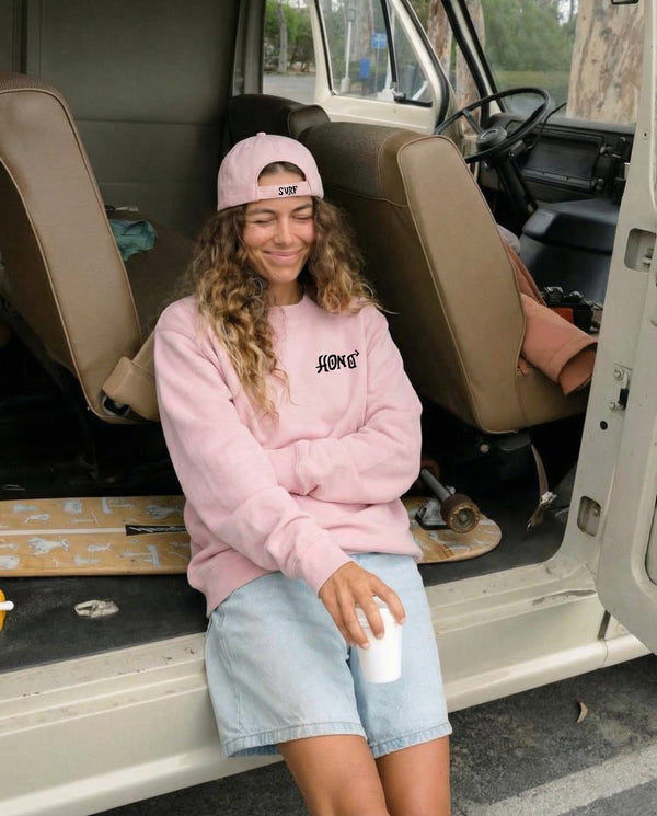 Femme portant un sweat rose HONO durable surfwear et une casquette surf rose, ambiance van life et lifestyle surf naturel.