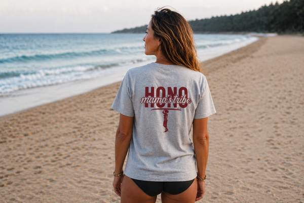 Femme portant un t-shirt surfwear gris chiné HONO Mama’s Tribe avec logo surf au dos sur la plage