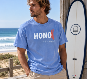 T-shirt HONO Surf bleu pour homme en coton bio, style vintage, porté avec une planche de surf sur la plage