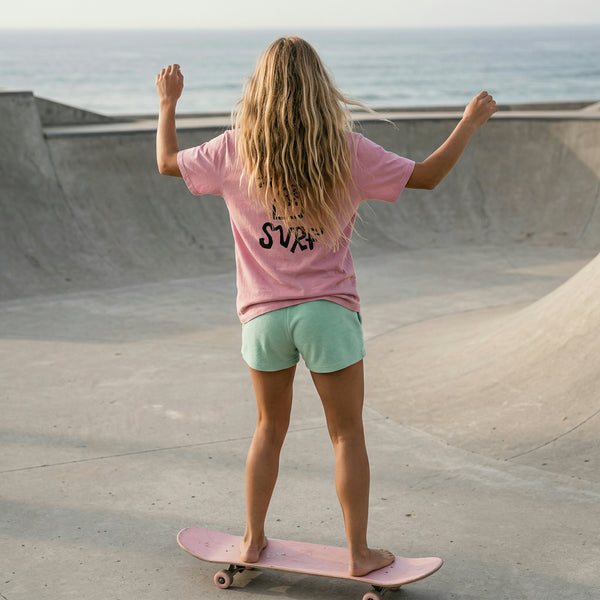 Femme portant le t-shirt surf HONO Tiki rose vintage en skatepark face à l’océan avec logo HONO SURF au dos