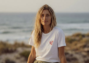 femme portant un t-shirt unisexe bio HONO blanc avec logo cœur surf corail au bord de la mer